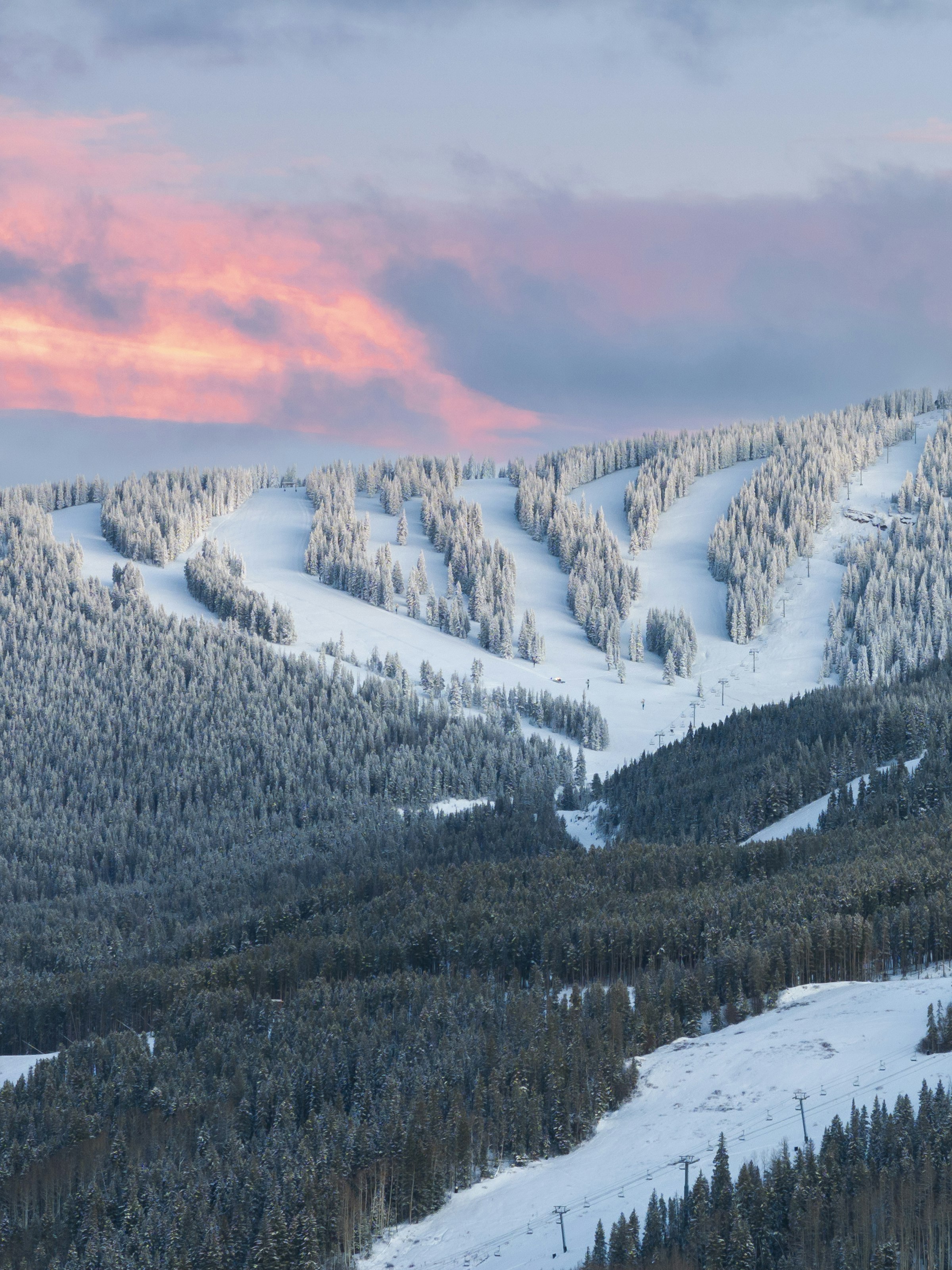 Tree-lined ski runs under a pink alpenglow sky